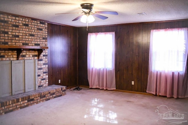 unfurnished living room with wood walls, ceiling fan, light carpet, and a textured ceiling