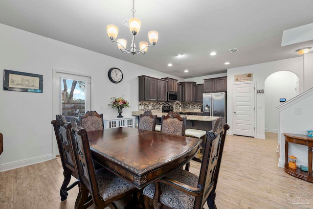 dining room featuring baseboards, visible vents, light wood-style flooring, arched walkways, and a chandelier