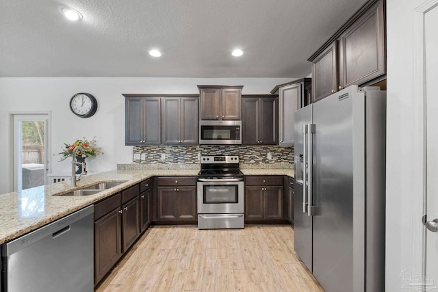 kitchen featuring a sink, backsplash, appliances with stainless steel finishes, light stone countertops, and dark brown cabinets