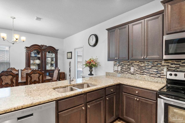 kitchen featuring dark brown cabinets, light stone countertops, a notable chandelier, stainless steel appliances, and a sink