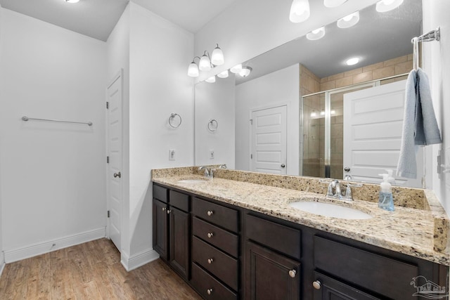 full bathroom with double vanity, a stall shower, wood finished floors, and a sink