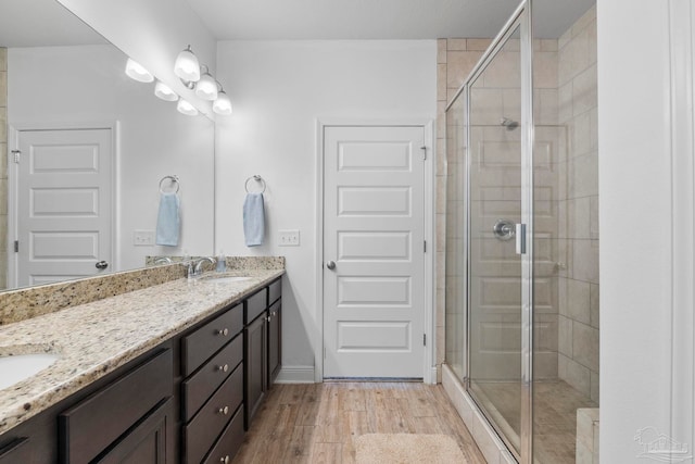 full bath featuring a stall shower, a sink, wood finished floors, double vanity, and baseboards