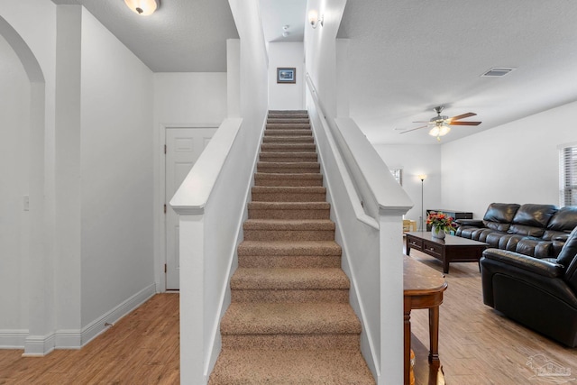 stairway featuring visible vents, a textured ceiling, wood finished floors, and a ceiling fan