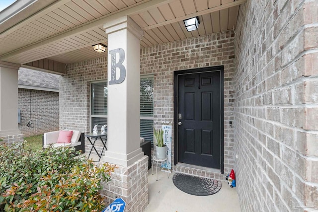 doorway to property featuring a porch and brick siding