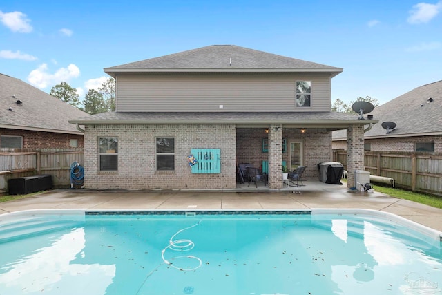 rear view of property with a fenced in pool, fence, a shingled roof, a patio area, and brick siding