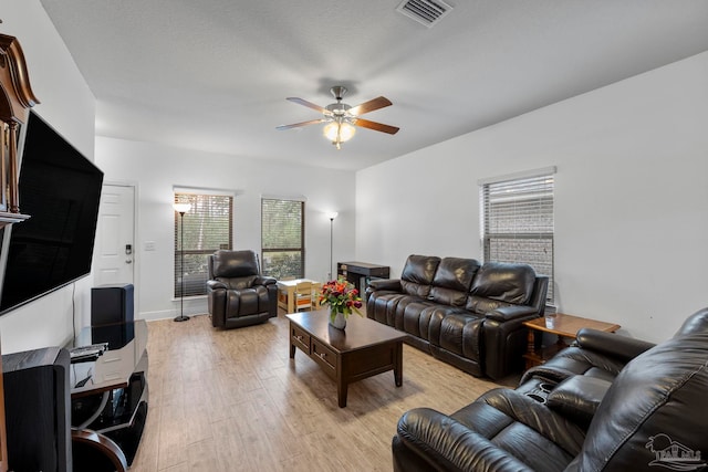 living room featuring light wood-style floors, visible vents, and ceiling fan