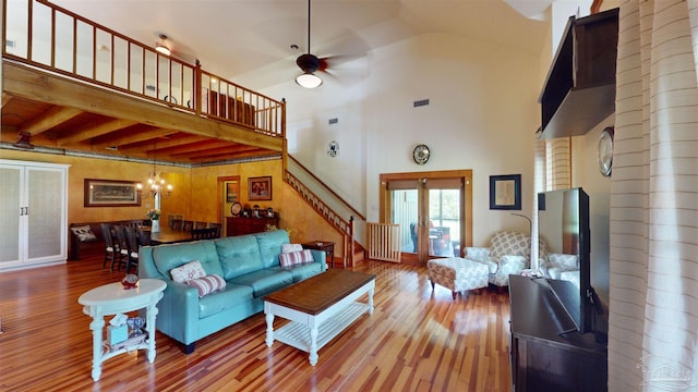 living room with hardwood / wood-style flooring, a high ceiling, ceiling fan with notable chandelier, beam ceiling, and french doors