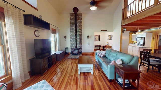 living room with wood-type flooring, ceiling fan, a high ceiling, a wood stove, and brick wall