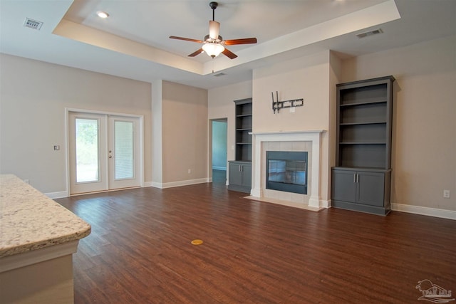living room with visible vents, built in features, a fireplace, a tray ceiling, and baseboards
