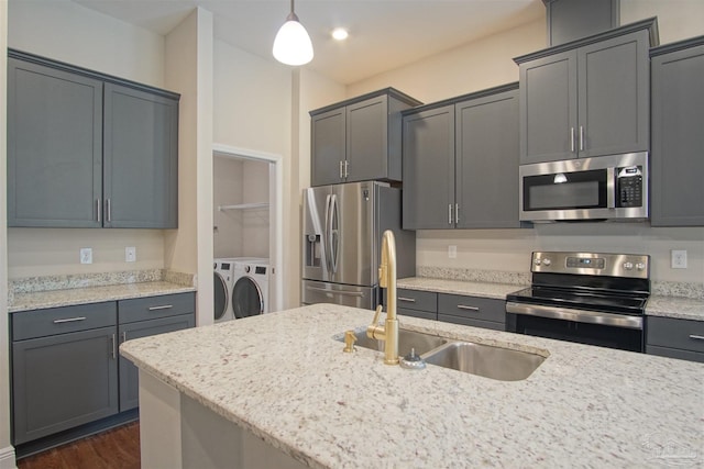 kitchen with light stone countertops, decorative light fixtures, a sink, washer and clothes dryer, and stainless steel appliances