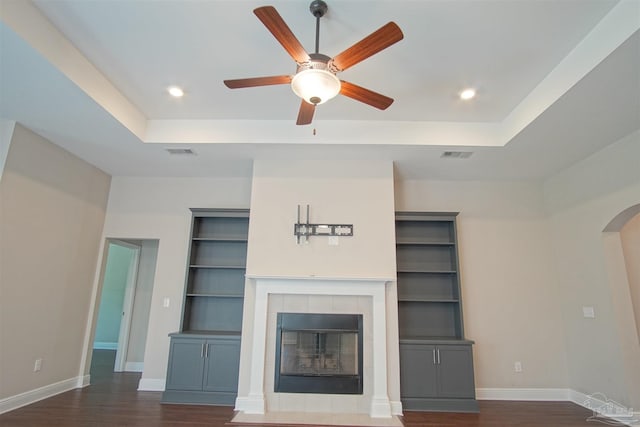 unfurnished living room with a tiled fireplace, visible vents, baseboards, and dark wood-style floors