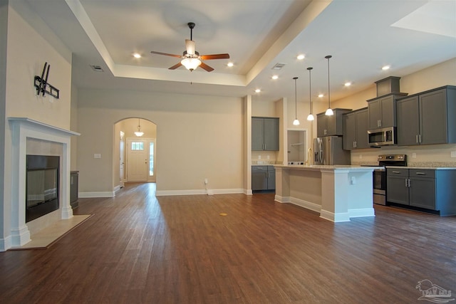 kitchen featuring open floor plan, a ceiling fan, a raised ceiling, gray cabinetry, and appliances with stainless steel finishes