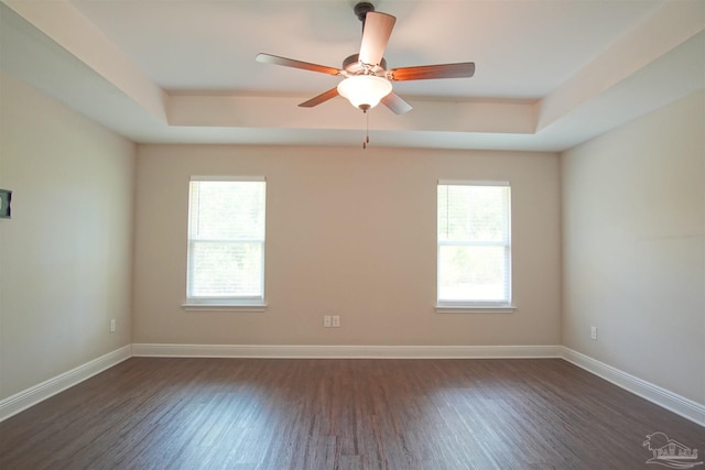 unfurnished room featuring dark wood finished floors, baseboards, a raised ceiling, and a healthy amount of sunlight
