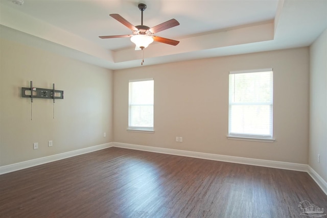 spare room featuring baseboards, a raised ceiling, ceiling fan, and dark wood-style floors
