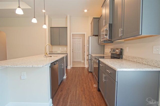 kitchen featuring light stone countertops, dark wood-style flooring, a sink, a kitchen island with sink, and appliances with stainless steel finishes