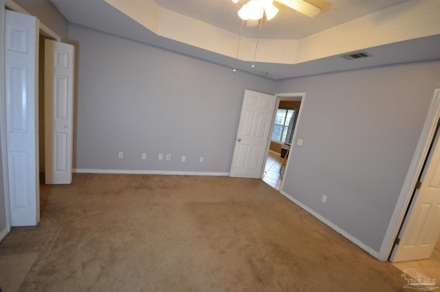 unfurnished bedroom featuring visible vents, carpet, baseboards, and a tray ceiling