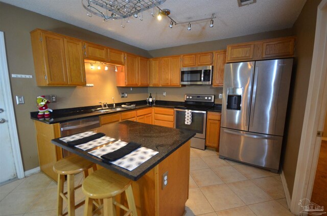 kitchen featuring light tile patterned flooring, dark countertops, appliances with stainless steel finishes, a sink, and baseboards