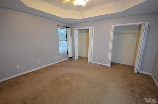 unfurnished bedroom with two closets, baseboards, carpet floors, and a raised ceiling