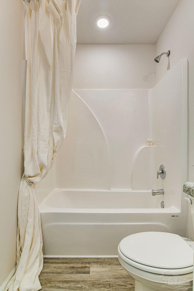 bathroom with hardwood / wood-style floors, shower / bath combination with curtain, toilet, and a textured ceiling