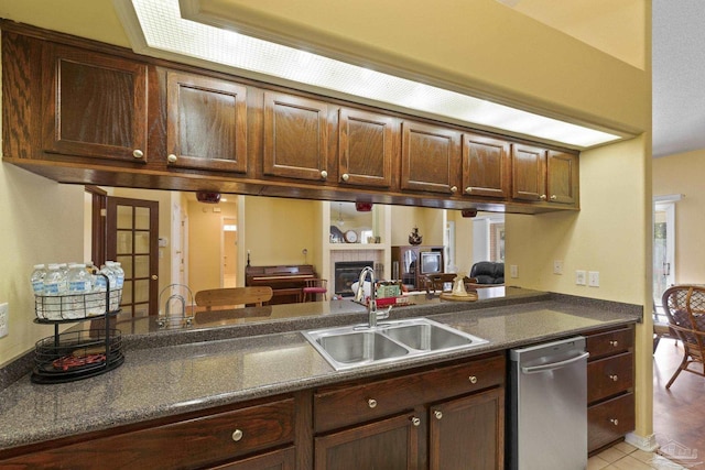 kitchen featuring a tiled fireplace, sink, dark brown cabinets, and dishwasher