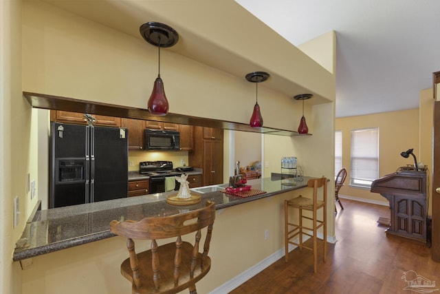 kitchen featuring dark stone countertops, hanging light fixtures, black appliances, and kitchen peninsula