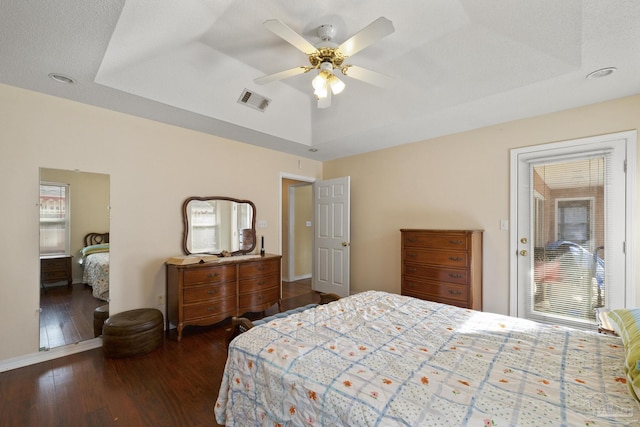 bedroom featuring dark hardwood / wood-style flooring, a tray ceiling, a textured ceiling, and ceiling fan