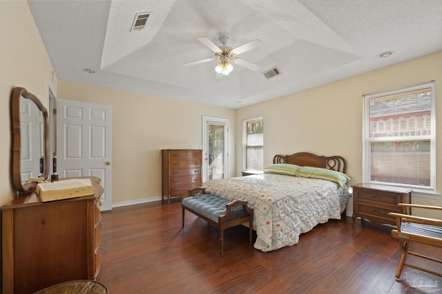 bedroom featuring dark hardwood / wood-style floors, a tray ceiling, multiple windows, and a textured ceiling