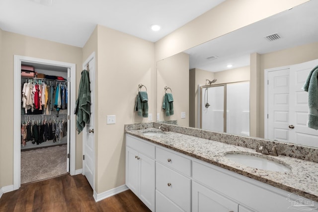 full bathroom with a stall shower, wood finished floors, visible vents, and a sink