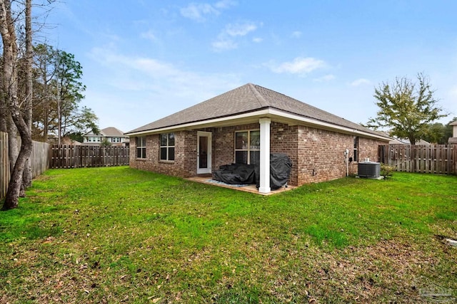 back of property featuring a yard, a fenced backyard, brick siding, and central AC