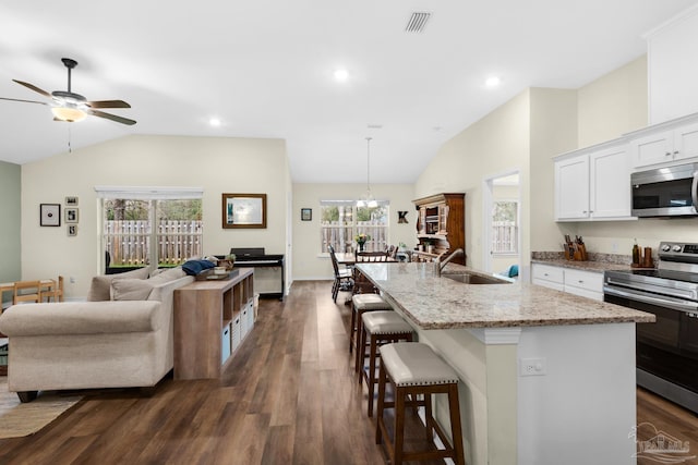 kitchen featuring a kitchen bar, lofted ceiling, light stone counters, appliances with stainless steel finishes, and a sink