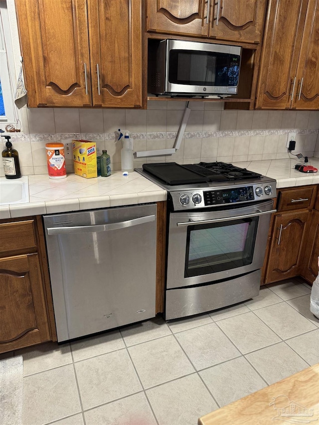 8156 Pompano St, Navarre, FL 32566 - kitchen featuring decorative backsplash, appliances with stainless steel finishes, light tile patterned flooring, and tile countertops