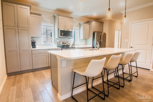 kitchen with stainless steel appliances, a sink, light wood-style flooring, and a center island with sink