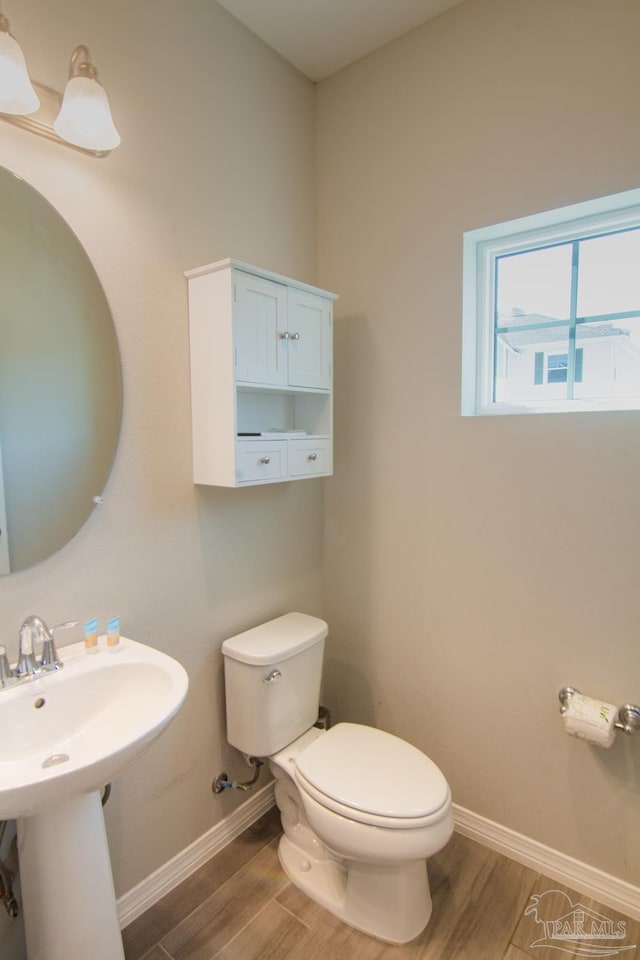 half bathroom with toilet, baseboards, and wood finished floors