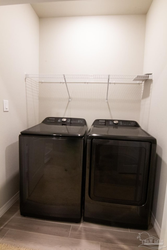 laundry area with laundry area, baseboards, wood finish floors, and washing machine and clothes dryer