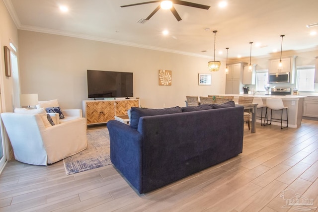 living room with ceiling fan, light wood finished floors, visible vents, and ornamental molding