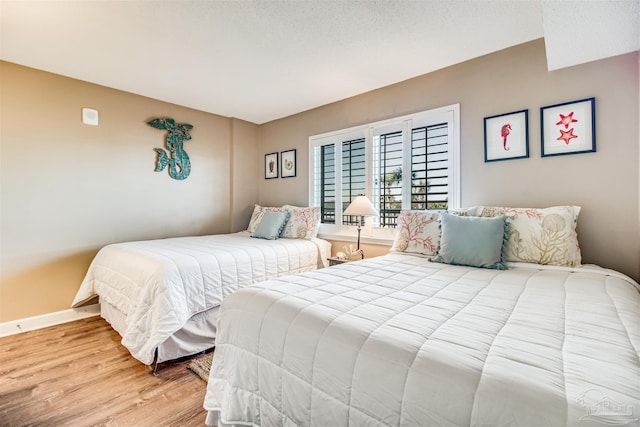 bedroom with light wood-style floors, a textured ceiling, and baseboards