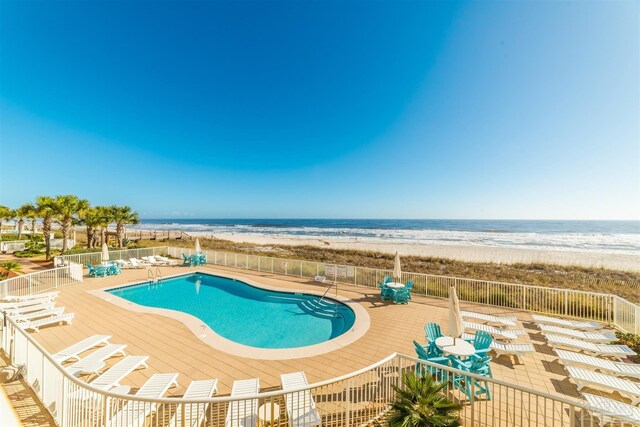 pool featuring a patio area, a water view, fence, and a beach view