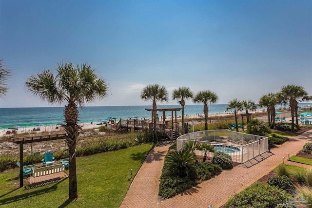 view of property's community with a beach view, a lawn, a water view, and a hot tub