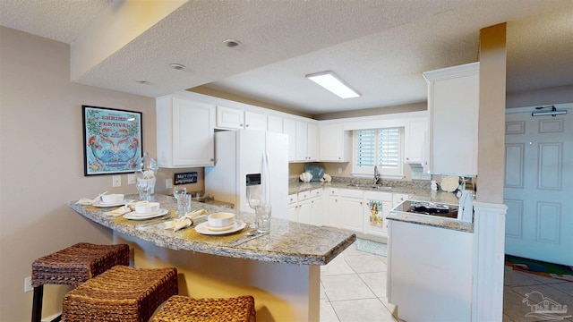 kitchen with light tile patterned floors, white refrigerator with ice dispenser, a kitchen breakfast bar, a peninsula, and a sink