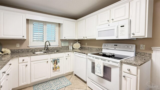 kitchen with light stone counters, light tile patterned floors, white cabinets, a sink, and white appliances