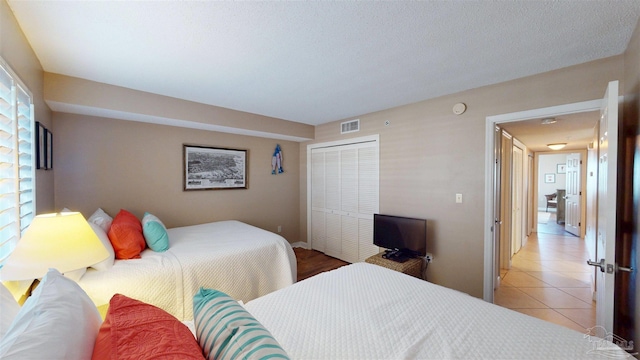 bedroom featuring light tile patterned floors, a textured ceiling, visible vents, and a closet