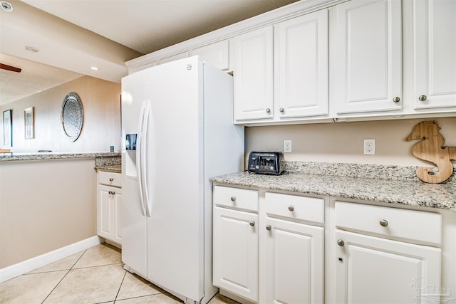 kitchen with white refrigerator with ice dispenser, light tile patterned flooring, white cabinetry, and baseboards