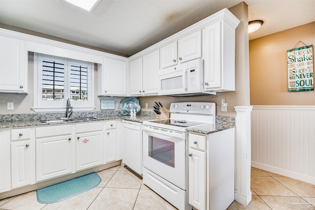 kitchen with white appliances, light tile patterned flooring, a sink, and a wainscoted wall