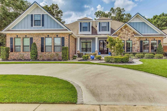 craftsman house with brick siding, board and batten siding, a front yard, and roof with shingles