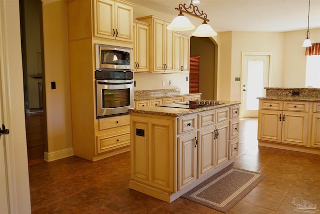 kitchen with light stone counters, pendant lighting, stainless steel appliances, and a kitchen island