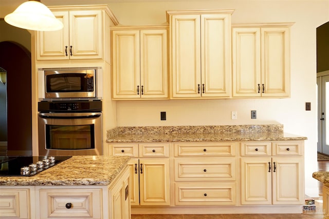 kitchen featuring light stone countertops, appliances with stainless steel finishes, decorative light fixtures, and cream cabinetry