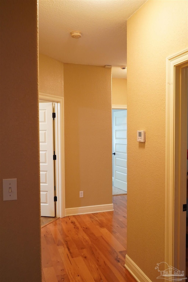 hall with a textured ceiling and light hardwood / wood-style floors