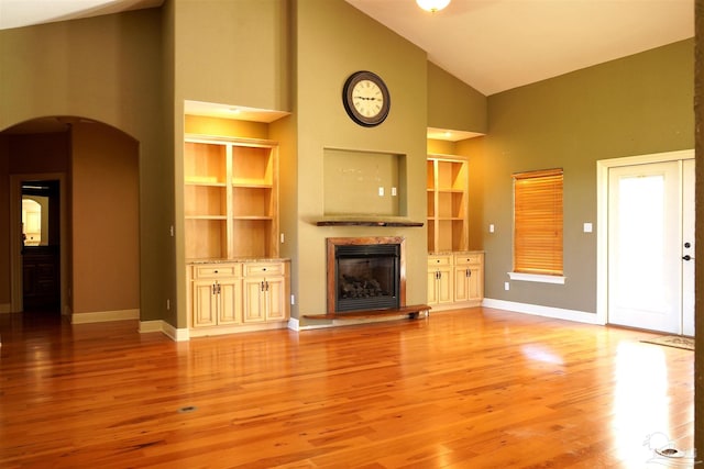 unfurnished living room featuring built in shelves, light hardwood / wood-style flooring, and high vaulted ceiling