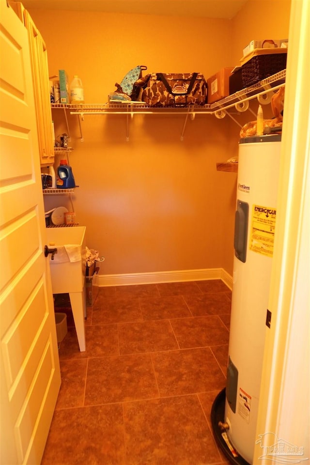 spacious closet featuring water heater and dark tile patterned flooring