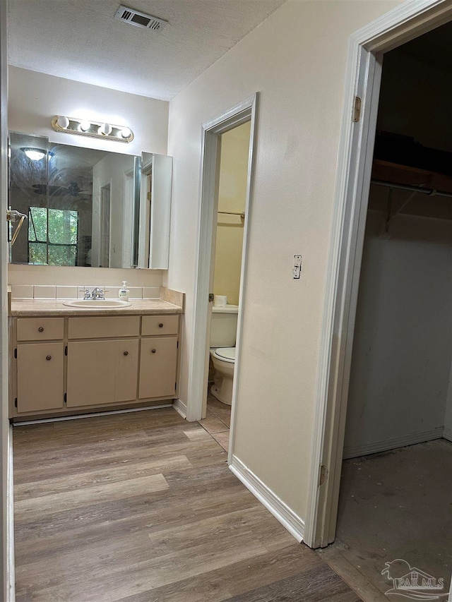 bathroom featuring wood-type flooring, a textured ceiling, vanity, and toilet